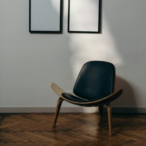 A modern armchair sits under two blank frames on an elegant wooden floor.