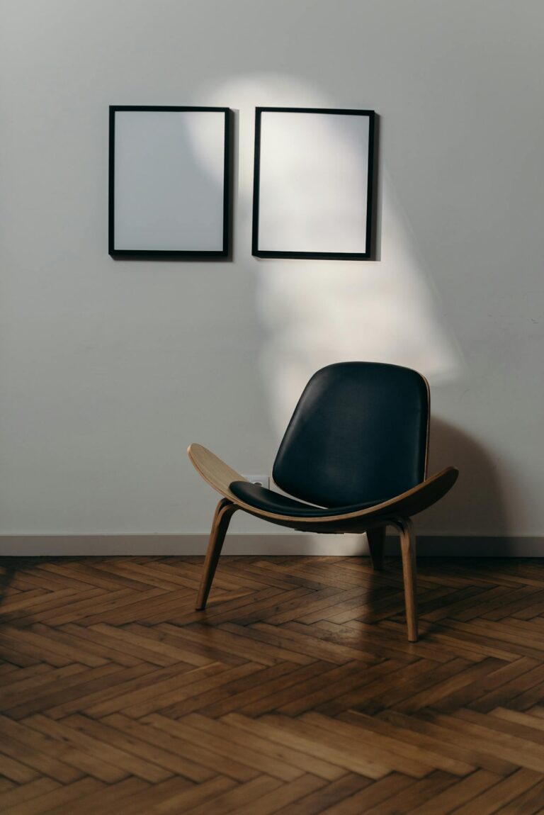 A modern armchair sits under two blank frames on an elegant wooden floor.