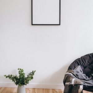 A simple, modern room with a blank frame, plant, and cozy chair.