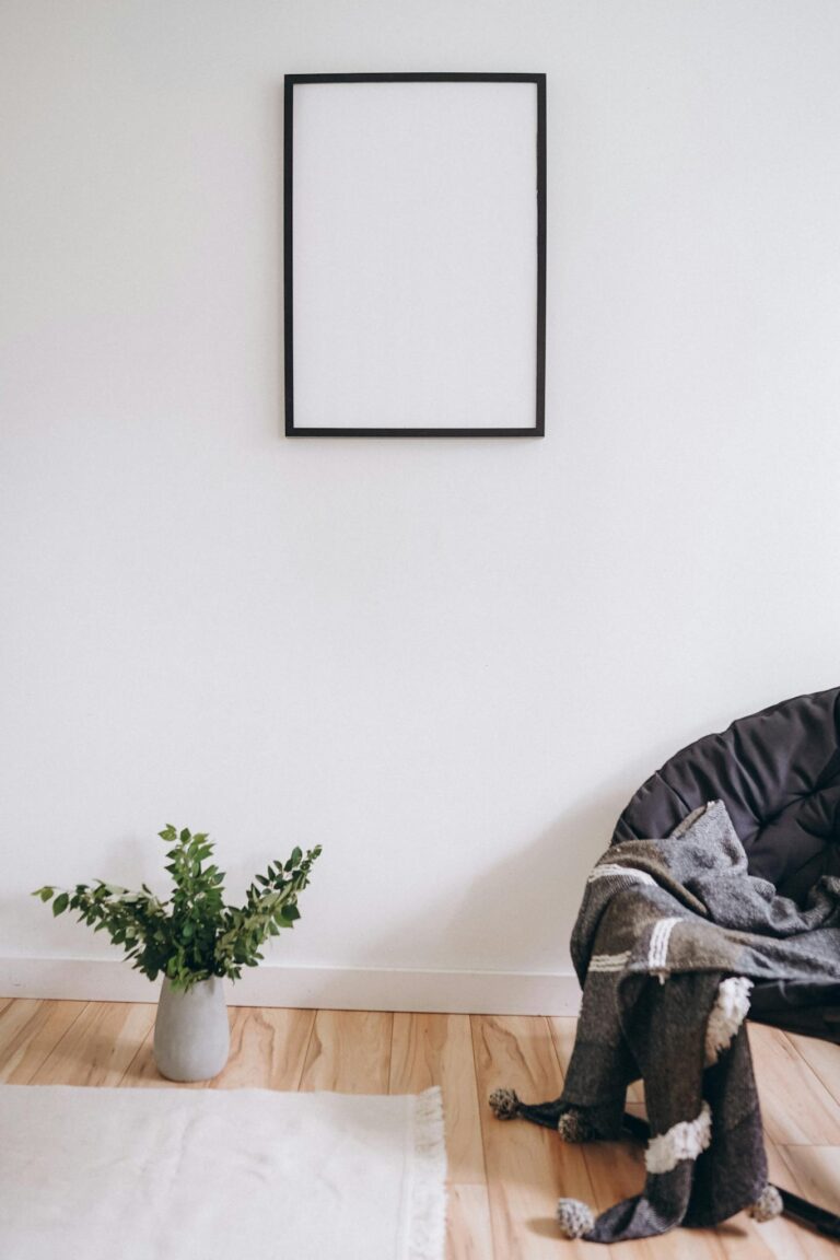 A simple, modern room with a blank frame, plant, and cozy chair.