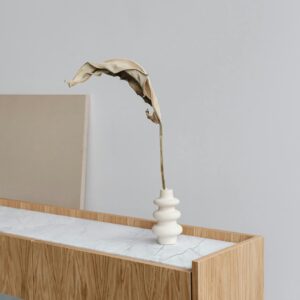 Modern minimalist interior featuring a dry leaf in a striking white vase on a stylish wooden console.