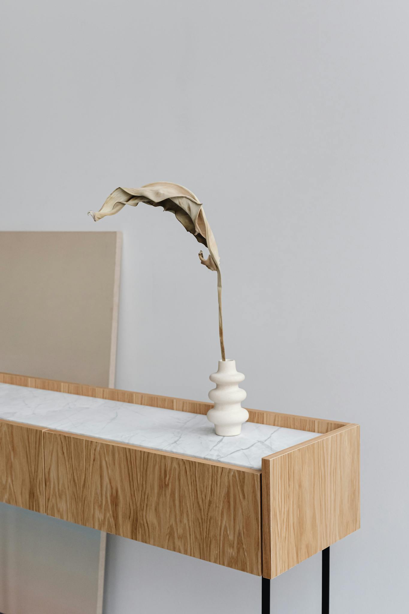 Modern minimalist interior featuring a dry leaf in a striking white vase on a stylish wooden console.